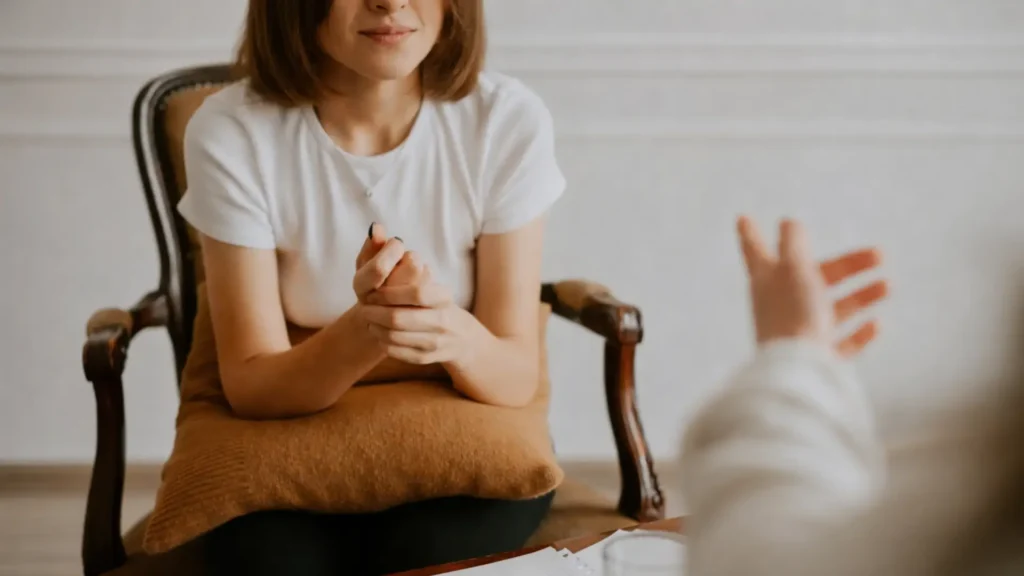 Partial view of a person seated on a wooden chair, holding a pillow