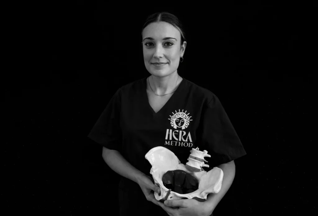Woman in Hera Method scrubs holds a pelvic bone model